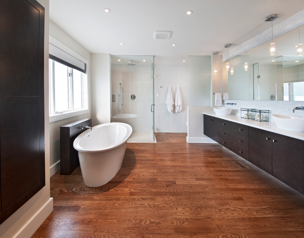 Design ideas for a large modern bathroom in Ottawa with a vessel sink, flat-panel cabinets, dark wood cabinets, engineered stone worktops, a freestanding bath, a built-in shower, a one-piece toilet, white tiles, grey walls and medium hardwood flooring.
