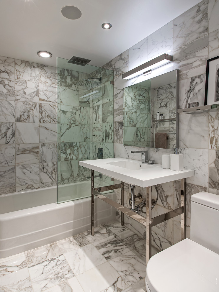 Inspiration for a medium sized contemporary shower room bathroom in New York with open cabinets, a built-in bath, a shower/bath combination, a two-piece toilet, grey tiles, stone tiles, grey walls, marble flooring, solid surface worktops and a console sink.