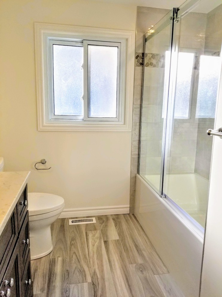 Inspiration for a medium sized classic bathroom in Toronto with recessed-panel cabinets, brown cabinets, an alcove shower, a one-piece toilet, multi-coloured tiles, pebble tiles, white walls, quartz worktops, brown floors, a sliding door, white worktops, a single sink and a built in vanity unit.