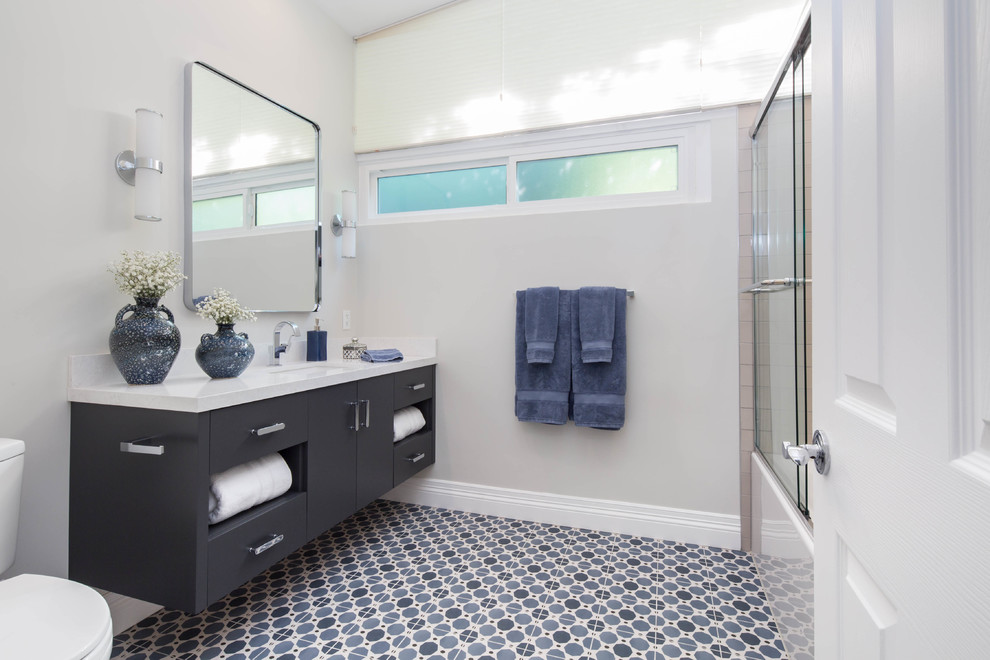 Réalisation d'une salle de bain design de taille moyenne avec un placard à porte plane, des portes de placard grises, une baignoire en alcôve, un combiné douche/baignoire, WC à poser, un carrelage gris, des carreaux de céramique, un mur gris, un sol en carrelage de céramique, un lavabo encastré, un plan de toilette en quartz modifié, un sol bleu, une cabine de douche à porte coulissante et un plan de toilette blanc.