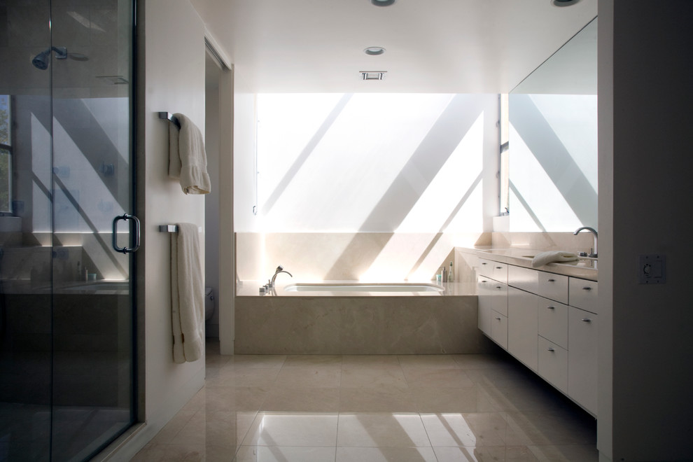 This is an example of a large modern bathroom in Los Angeles with flat-panel cabinets, white cabinets, a corner bath, a walk-in shower, a one-piece toilet, ceramic tiles, beige walls, ceramic flooring, a built-in sink, soapstone worktops and grey floors.