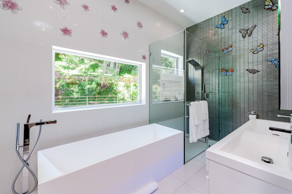 This is an example of a medium sized contemporary family bathroom in Los Angeles with a freestanding bath, an integrated sink, solid surface worktops, white floors, a hinged door, flat-panel cabinets, white cabinets, an alcove shower, multi-coloured walls, black tiles and matchstick tiles.