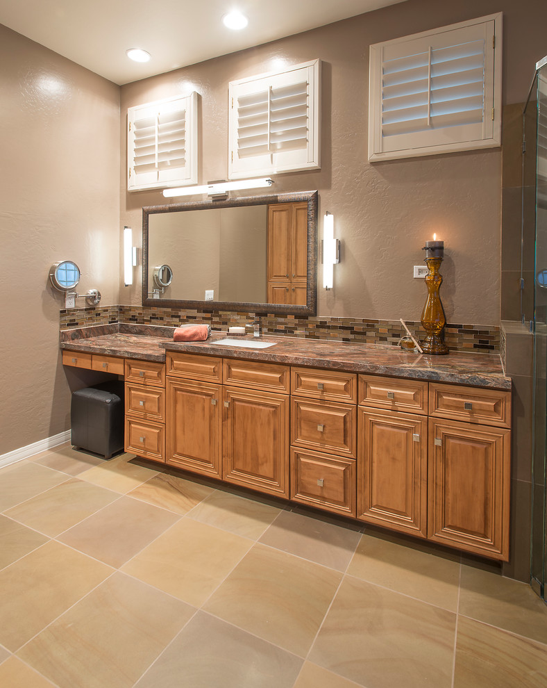 Example of a large trendy master brown tile and glass sheet limestone floor bathroom design in Phoenix with an undermount sink, raised-panel cabinets, medium tone wood cabinets, granite countertops, a two-piece toilet and beige walls