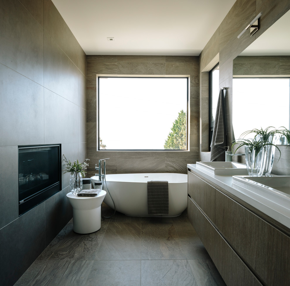 This is an example of a large contemporary ensuite bathroom in Vancouver with flat-panel cabinets, a freestanding bath, grey tiles, porcelain tiles, porcelain flooring, engineered stone worktops, grey floors, white worktops, dark wood cabinets and a built-in sink.