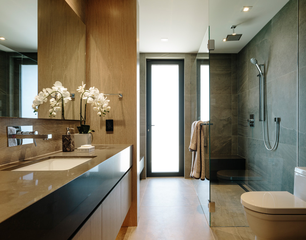 Idée de décoration pour une grande salle de bain design en bois brun avec un placard à porte plane, une douche à l'italienne, un carrelage gris, des carreaux de porcelaine, un mur gris, un sol en carrelage de porcelaine, un lavabo encastré, un plan de toilette en quartz modifié, un sol gris, une cabine de douche à porte battante et un plan de toilette gris.