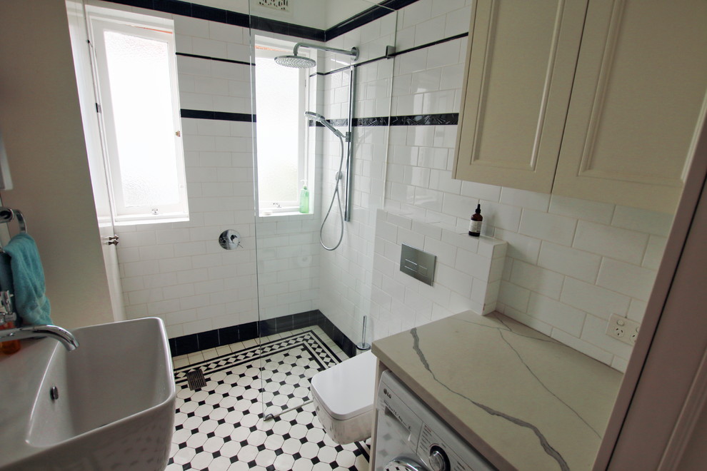 This is an example of a medium sized traditional ensuite bathroom in Sydney with recessed-panel cabinets, white cabinets, a corner bath, a walk-in shower, a wall mounted toilet, black and white tiles, ceramic tiles, white walls, ceramic flooring, a wall-mounted sink, engineered stone worktops, white floors, an open shower and white worktops.