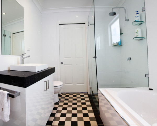 Example of a mid-sized trendy ceramic tile ceramic tile bathroom design in Sydney with a trough sink, flat-panel cabinets, white cabinets, marble countertops, a one-piece toilet and white walls