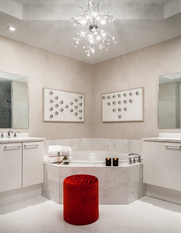 Modern inredning av ett stort en-suite badrum, med ett undermonterad handfat, släta luckor, vita skåp, marmorbänkskiva, ett hörnbadkar, en hörndusch, en toalettstol med separat cisternkåpa, vit kakel, porslinskakel, grå väggar och klinkergolv i porslin