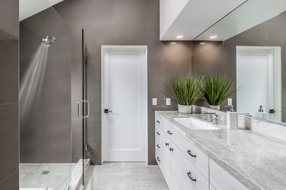 Idée de décoration pour une salle de bain principale design de taille moyenne avec un placard à porte plane, des portes de placard grises, un plan de toilette en quartz, une douche d'angle, un mur gris, un sol en marbre, un lavabo encastré, un sol gris et une cabine de douche à porte battante.