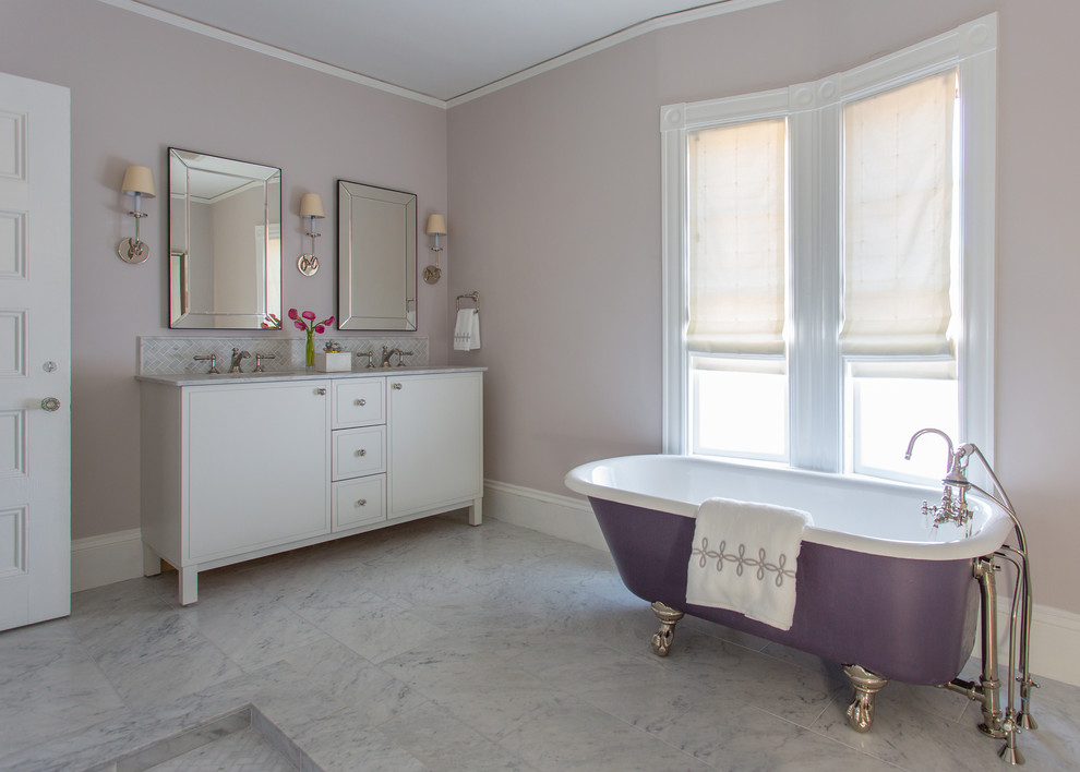 Réalisation d'une salle de bain principale tradition de taille moyenne avec des portes de placard blanches, une baignoire sur pieds, un plan de toilette en marbre, un placard à porte plane, un mur violet, un lavabo encastré et un carrelage blanc.