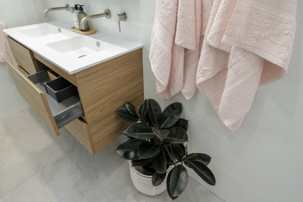 Réalisation d'une petite salle de bain principale nordique en bois clair avec une baignoire d'angle, une douche d'angle, un lavabo intégré, une cabine de douche à porte battante, un plan de toilette blanc, meuble double vasque et meuble-lavabo suspendu.