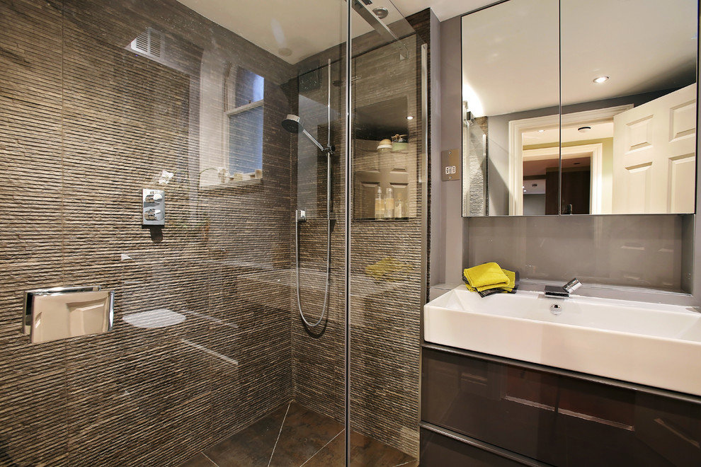 Exemple d'une petite salle d'eau tendance avec un placard à porte plane, des portes de placard grises, une douche ouverte, WC suspendus, un carrelage gris, un carrelage de pierre, un mur gris, un sol en carrelage de céramique et une grande vasque.