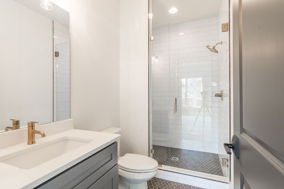 На фото: детская ванная комната среднего размера в стиле неоклассика (современная классика) с фасадами в стиле шейкер, серыми фасадами, двойным душем, унитазом-моноблоком, белой плиткой, плиткой кабанчик, белыми стенами, полом из мозаичной плитки, накладной раковиной, столешницей из искусственного кварца, серым полом, душем с распашными дверями, белой столешницей, тумбой под одну раковину, встроенной тумбой и кирпичными стенами с