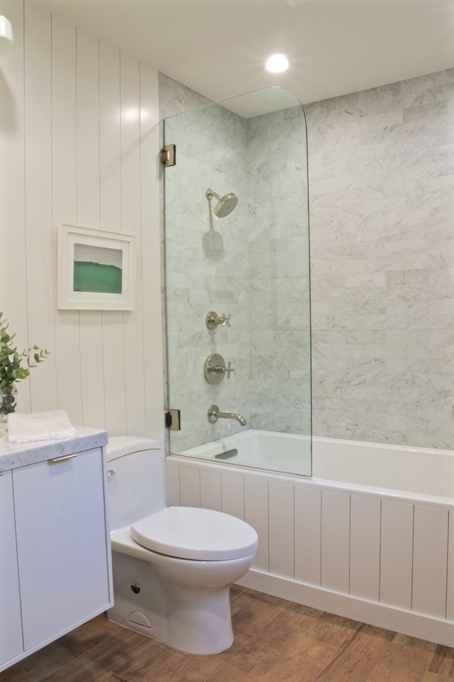 ロサンゼルスにあるお手頃価格の小さなビーチスタイルのおしゃれな浴室 (フラットパネル扉のキャビネット、白いキャビネット、アルコーブ型浴槽、アルコーブ型シャワー、一体型トイレ	、白いタイル、大理石タイル、白い壁、無垢フローリング、アンダーカウンター洗面器、大理石の洗面台、茶色い床、オープンシャワー、白い洗面カウンター) の写真