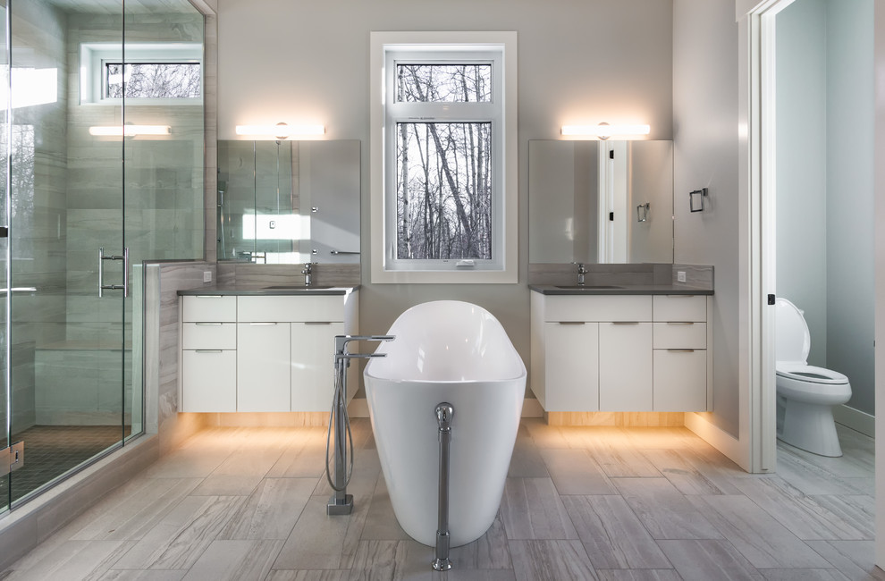 Inspiration for a large traditional ensuite bathroom in Edmonton with flat-panel cabinets, white cabinets, a freestanding bath, a double shower, a one-piece toilet, grey tiles, ceramic tiles, grey walls, ceramic flooring, a built-in sink, tiled worktops, grey floors, a hinged door and grey worktops.