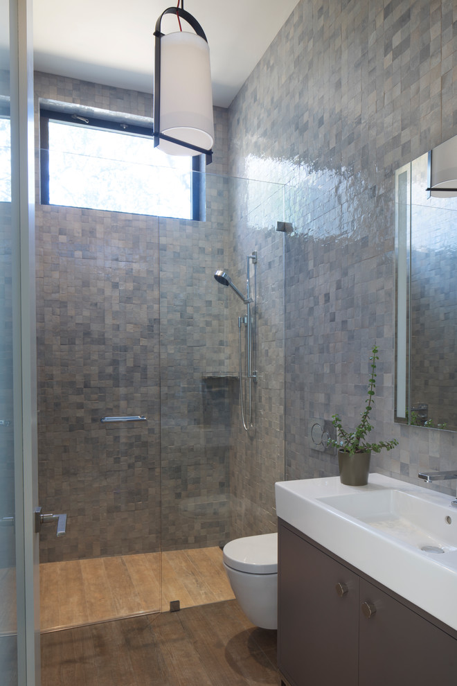 Design ideas for a medium sized modern shower room bathroom in San Luis Obispo with recessed-panel cabinets, grey cabinets, a built-in shower, a wall mounted toilet, blue tiles, ceramic tiles, blue walls, ceramic flooring, an integrated sink, solid surface worktops, beige floors, a hinged door and white worktops.