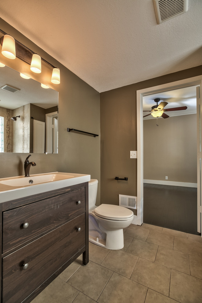 Example of a transitional porcelain tile bathroom design in Omaha with a trough sink, flat-panel cabinets, dark wood cabinets, solid surface countertops, a one-piece toilet and beige walls