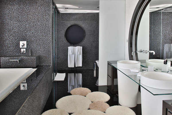 Immagine di una grande stanza da bagno padronale minimalista con lavabo a consolle, ante lisce, ante nere, top in vetro, vasca da incasso, piastrelle nere, piastrelle di vetro e pareti bianche