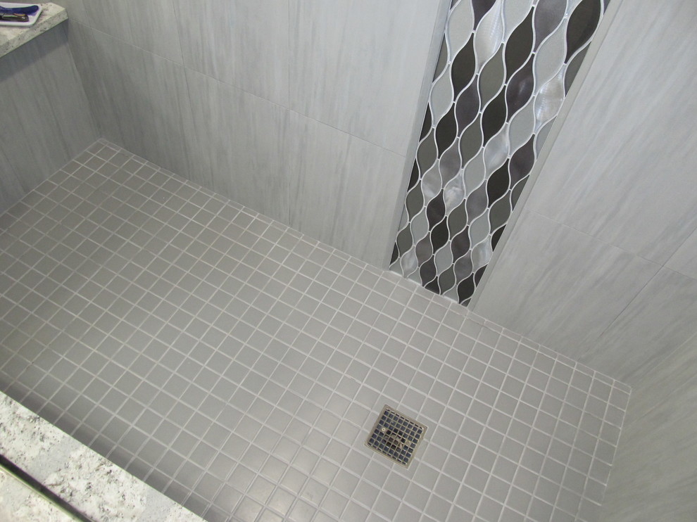 Cette photo montre une grande salle de bain principale tendance avec un placard avec porte à panneau encastré, des portes de placard grises, une baignoire indépendante, une douche d'angle, un carrelage blanc, un mur gris, un sol en carrelage de porcelaine, un lavabo encastré et un plan de toilette en quartz modifié.