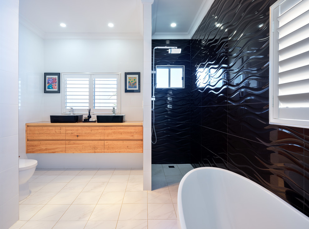 На фото: главная ванная комната среднего размера в современном стиле с фасадами островного типа, светлыми деревянными фасадами, отдельно стоящей ванной, душем в нише, унитазом-моноблоком, черно-белой плиткой, керамогранитной плиткой, полом из керамогранита, настольной раковиной, белым полом и открытым душем с