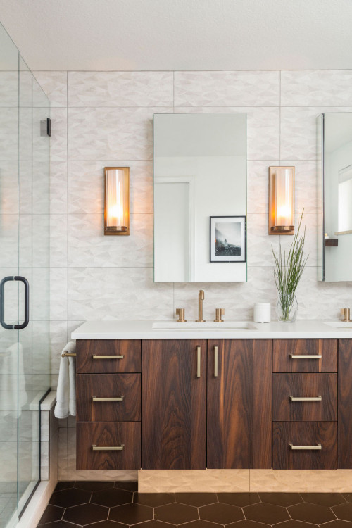 Modern bathroom cabinets with walnut wood grain, flat-front doors and drawers, brass hardware, white quartz countertop, frameless mirror, and glass shower beside.