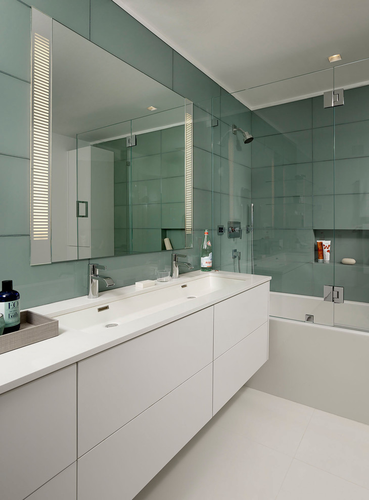 Modern inredning av ett mellanstort en-suite badrum, med släta luckor, vita skåp, ett badkar i en alkov, en dusch/badkar-kombination, grå kakel, grön kakel, glaskakel, gröna väggar, klinkergolv i porslin, ett avlångt handfat och bänkskiva i akrylsten