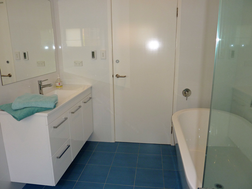 На фото: ванная комната в современном стиле с монолитной раковиной, отдельно стоящей ванной, угловым душем, плоскими фасадами, белыми фасадами, столешницей из искусственного камня, белой плиткой и керамогранитной плиткой с