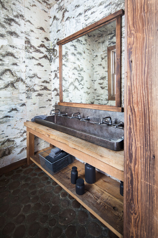 Exemple d'une grande salle d'eau montagne en bois brun avec une grande vasque, un placard sans porte, un sol en galet, un plan de toilette en bois, un carrelage de pierre, un mur multicolore et un plan de toilette marron.
