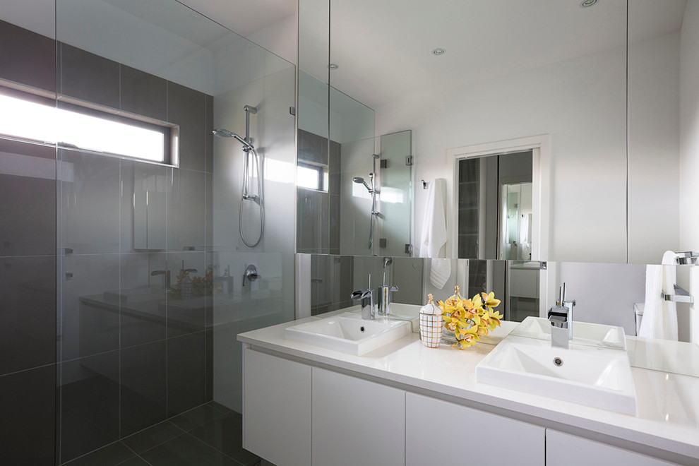 This is an example of a large contemporary ensuite bathroom in Melbourne with flat-panel cabinets, white cabinets, a double shower, a one-piece toilet, grey tiles, porcelain tiles, white walls, ceramic flooring, a wall-mounted sink, engineered stone worktops, grey floors and a hinged door.