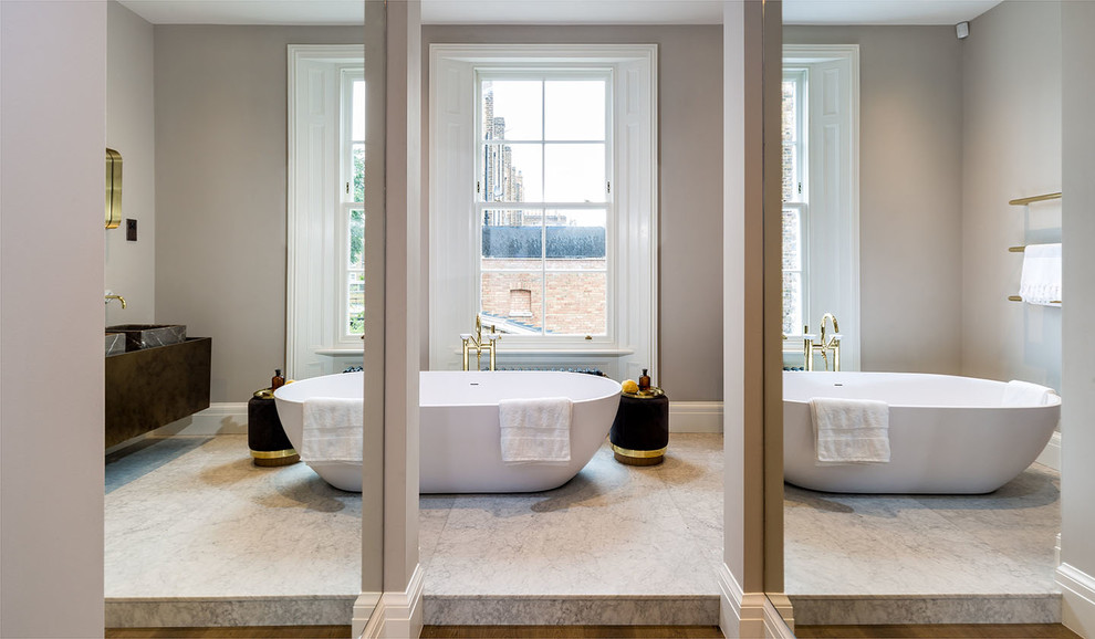 This is an example of a medium sized contemporary ensuite bathroom in London with medium wood cabinets, a freestanding bath, stone tiles, white walls, marble flooring, a trough sink and wooden worktops.