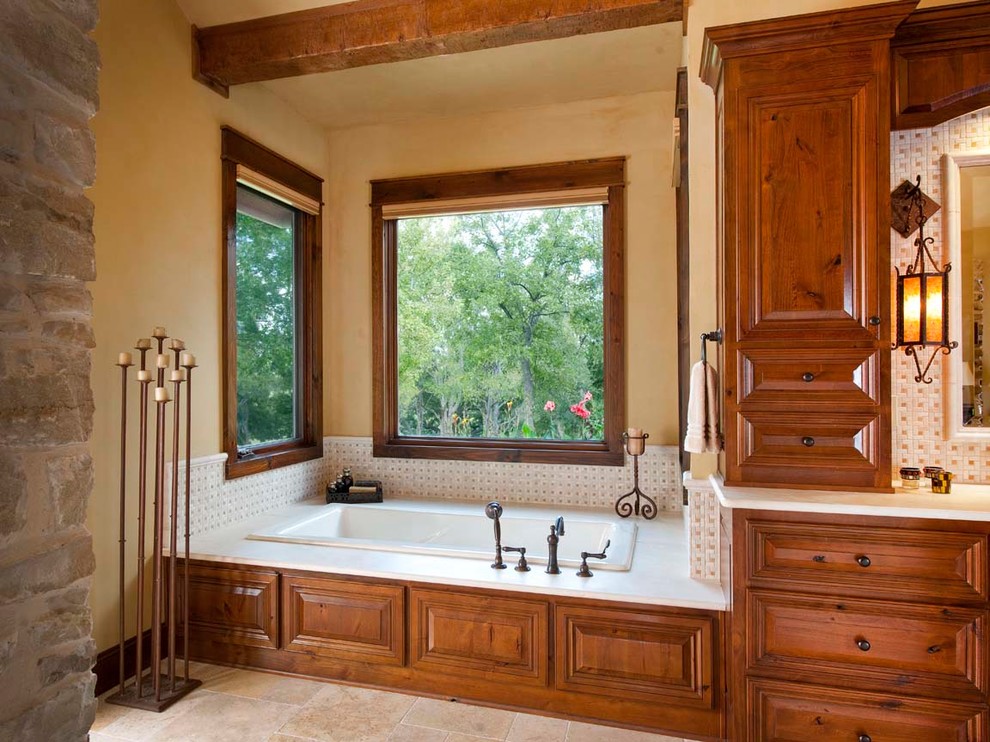 Cette photo montre une salle de bain montagne en bois brun avec un placard avec porte à panneau surélevé, une baignoire posée et un carrelage beige.