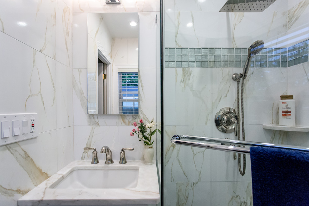 Inredning av ett modernt litet en-suite badrum, med ett undermonterad handfat, släta luckor, vita skåp, marmorbänkskiva, en hörndusch, vit kakel, porslinskakel, vita väggar och klinkergolv i porslin