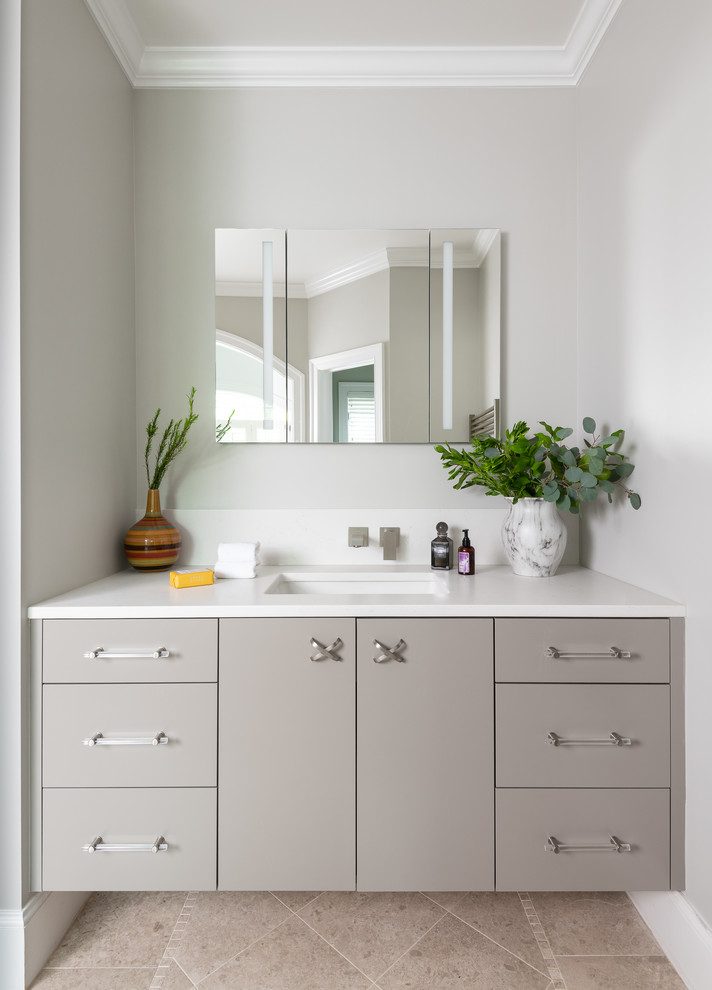 Cette photo montre une salle de bain tendance avec un placard à porte plane, des portes de placard grises, un mur gris, un lavabo encastré, un sol beige et un plan de toilette blanc.