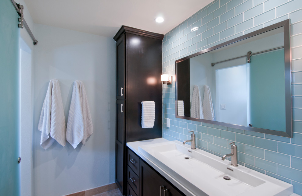 Exemple d'une grande salle de bain chic en bois foncé avec un placard avec porte à panneau encastré, un carrelage bleu, un carrelage métro, un mur bleu, une grande vasque, un plan de toilette en surface solide, une cabine de douche à porte coulissante, un plan de toilette blanc, meuble double vasque et meuble-lavabo encastré.