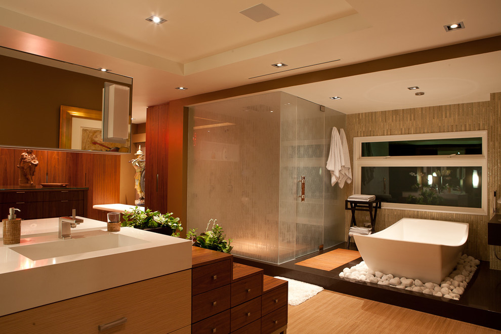 Inspiration for an expansive world-inspired ensuite bathroom in Los Angeles with flat-panel cabinets, light wood cabinets, a freestanding bath, a corner shower, brown tiles, ceramic tiles, brown walls, light hardwood flooring, an integrated sink, solid surface worktops and a hinged door.