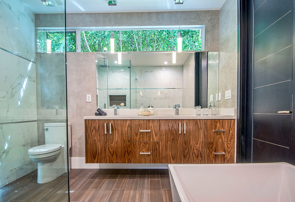 Large modern ensuite bathroom in Los Angeles with flat-panel cabinets, medium wood cabinets, a corner shower, a two-piece toilet, white tiles, porcelain tiles, white walls, porcelain flooring, a submerged sink, a hinged door, a freestanding bath, solid surface worktops and brown floors.