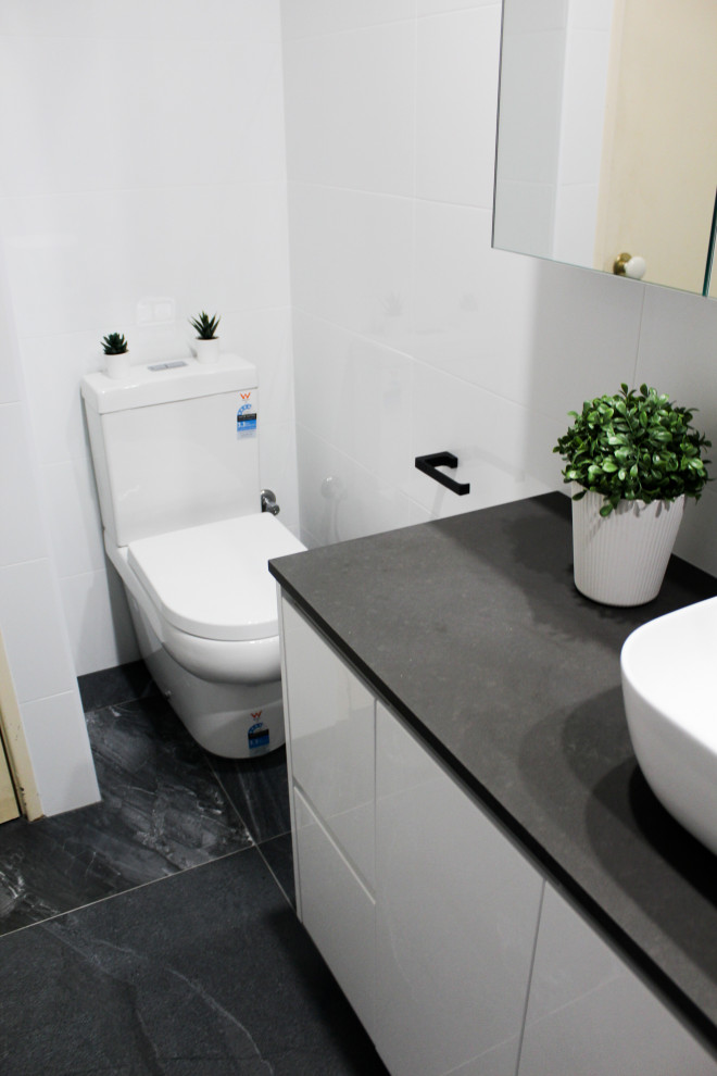Idéer för små funkis grått en-suite badrum, med släta luckor, vita skåp, en öppen dusch, en toalettstol med hel cisternkåpa, vit kakel, keramikplattor, svarta väggar, klinkergolv i porslin, ett fristående handfat, bänkskiva i kvarts, grått golv och med dusch som är öppen
