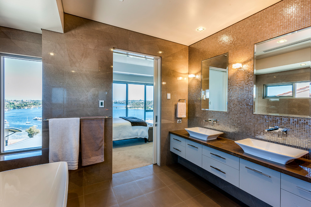 На фото: большая главная ванная комната в современном стиле с настольной раковиной, белыми фасадами, мраморной столешницей, коричневой плиткой и коричневыми стенами с