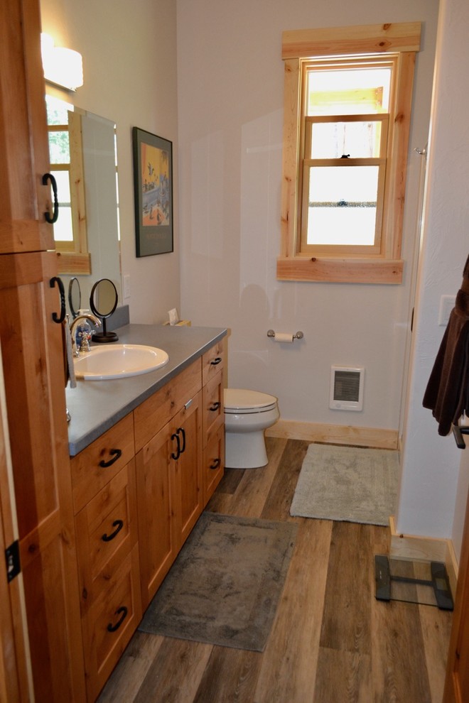 Réalisation d'une salle de bain chalet en bois brun de taille moyenne avec un placard à porte shaker, sol en stratifié, un lavabo posé, un plan de toilette en surface solide et un sol beige.