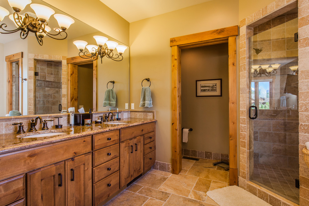 Aménagement d'une grande salle de bain principale montagne en bois brun avec un placard à porte affleurante, une baignoire posée, une douche d'angle, un carrelage beige, un carrelage de pierre, un mur beige, un sol en travertin, un lavabo encastré et un plan de toilette en granite.