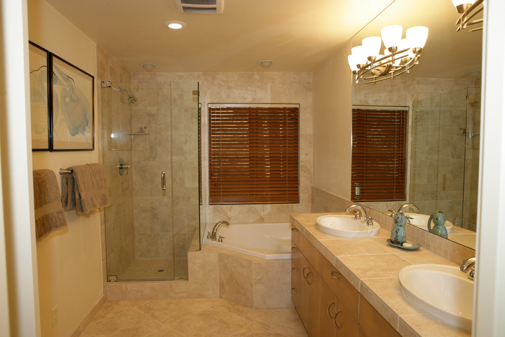 Réalisation d'une grande salle de bain principale minimaliste en bois clair avec un lavabo posé, un placard à porte affleurante, un plan de toilette en carrelage, une baignoire d'angle, une douche d'angle, un carrelage beige, un carrelage de pierre, un mur beige et un sol en carrelage de céramique.