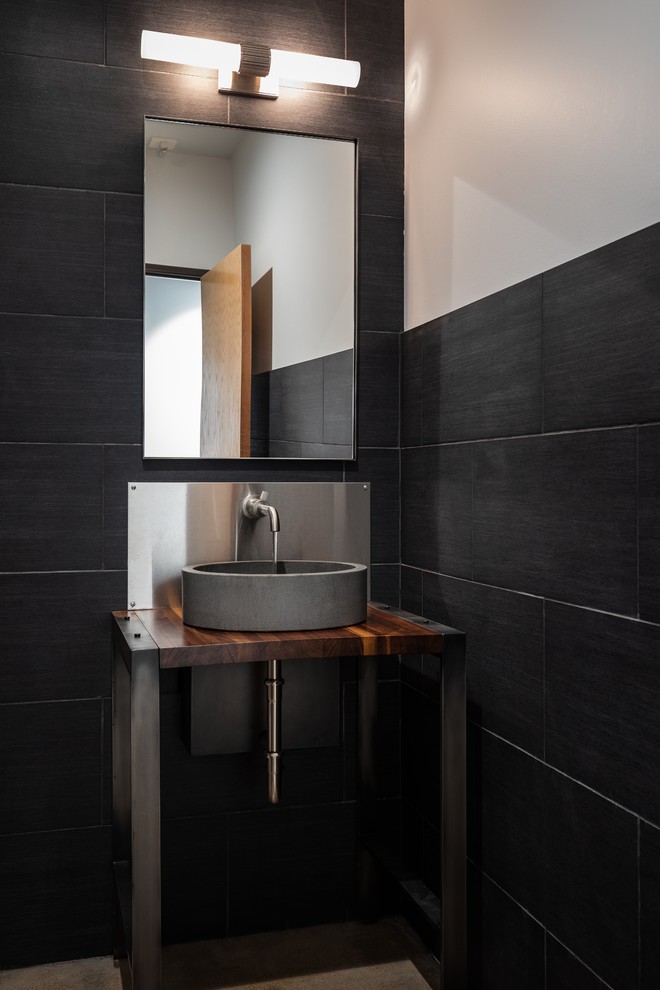 Inspiration pour une salle d'eau urbaine en bois brun de taille moyenne avec un placard sans porte, WC à poser, un carrelage noir, des carreaux de céramique, un mur noir, sol en béton ciré, une vasque, un plan de toilette en bois, un sol gris et un plan de toilette marron.