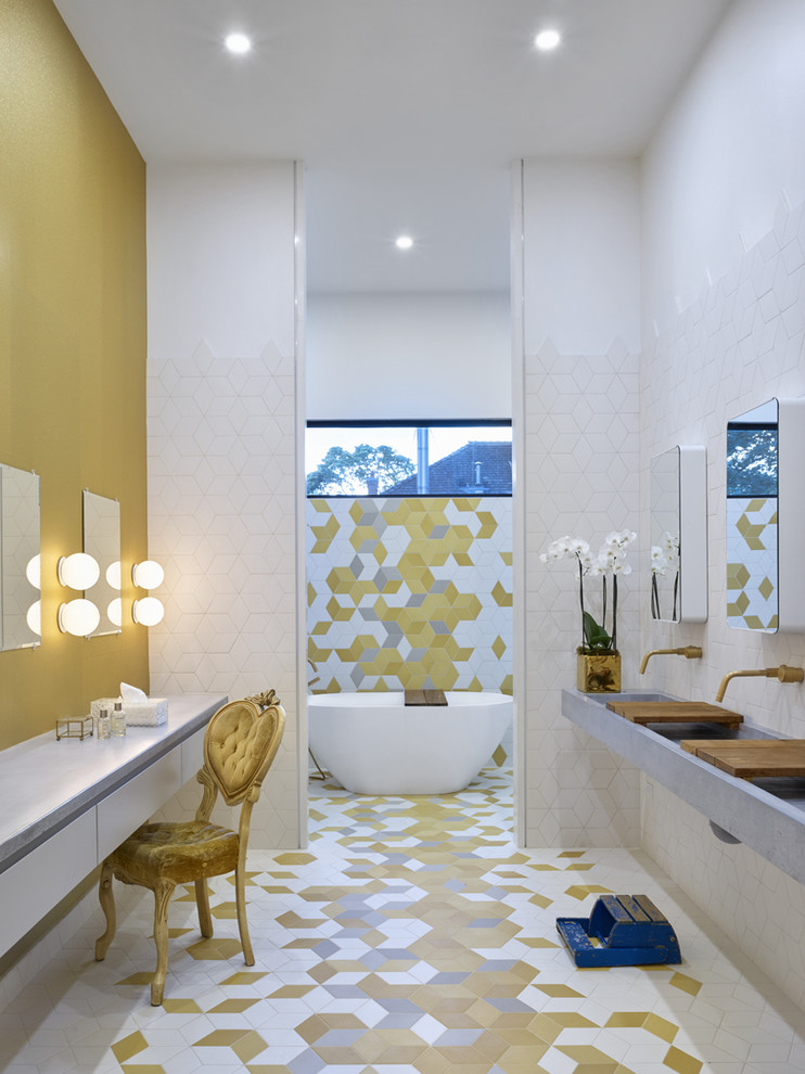 Imagen de cuarto de baño contemporáneo con armarios con paneles lisos, puertas de armario blancas, bañera exenta, baldosas y/o azulejos blancos, lavabo integrado, encimera de cemento y suelo multicolor
