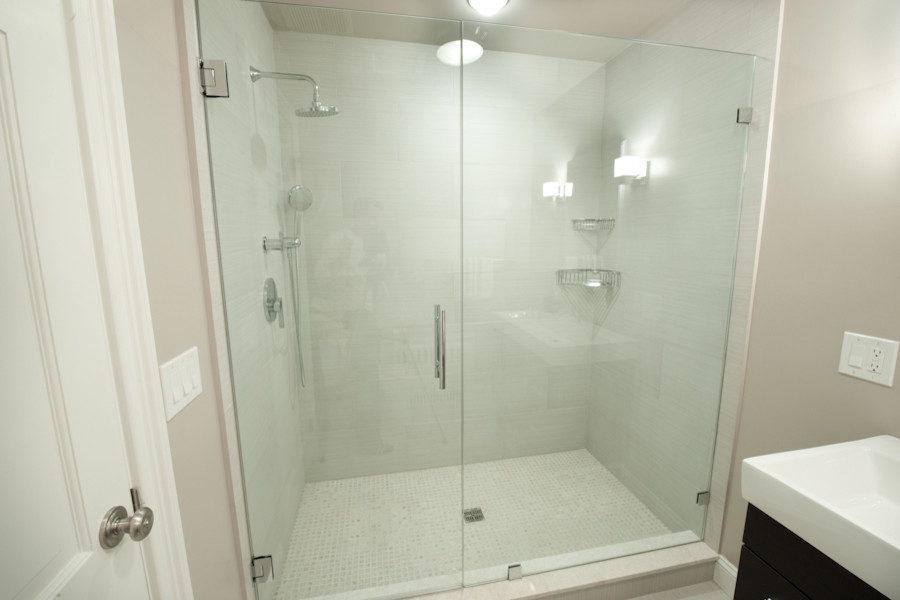 Example of a transitional white tile and stone tile tub/shower combo design in New York with an undermount sink, furniture-like cabinets, dark wood cabinets, glass countertops and a one-piece toilet