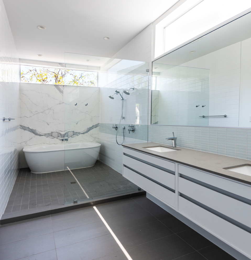 Exempel på ett mellanstort modernt grå grått en-suite badrum, med släta luckor, vita skåp, ett fristående badkar, en dusch/badkar-kombination, en vägghängd toalettstol, vit kakel, stenhäll, vita väggar, klinkergolv i porslin, ett undermonterad handfat, bänkskiva i kvarts, grått golv och med dusch som är öppen