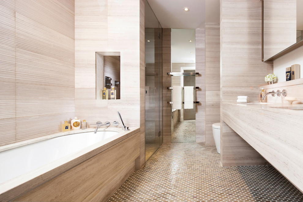 Medium sized modern ensuite bathroom in London with open cabinets, a built-in bath, a built-in shower, a wall mounted toilet, beige tiles, stone slabs, beige walls, mosaic tile flooring, a built-in sink, limestone worktops, beige floors and a hinged door.