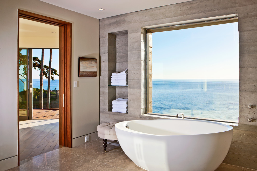 Cette image montre une grande salle de bain principale marine avec une baignoire indépendante, un mur gris, des carreaux de béton, un sol en calcaire et un sol beige.