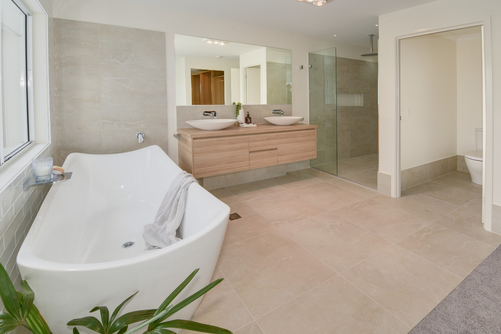 Свежая идея для дизайна: главная ванная комната в морском стиле с фасадами островного типа, светлыми деревянными фасадами, отдельно стоящей ванной, открытым душем, унитазом-моноблоком, бежевой плиткой, керамической плиткой, белыми стенами, полом из керамической плитки, настольной раковиной, бежевым полом, открытым душем и коричневой столешницей - отличное фото интерьера