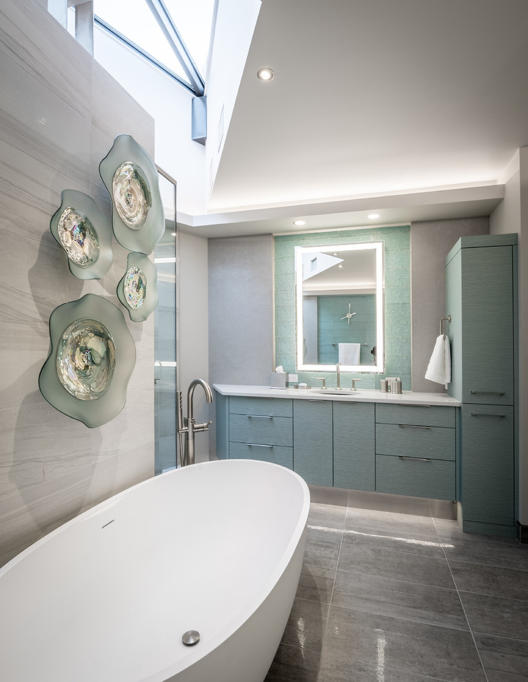 Inspiration for a contemporary ensuite bathroom in Other with freestanding cabinets, turquoise cabinets, a freestanding bath, a double shower, a one-piece toilet, green tiles, glass tiles, grey walls, ceramic flooring, a submerged sink, engineered stone worktops, grey floors and a hinged door.