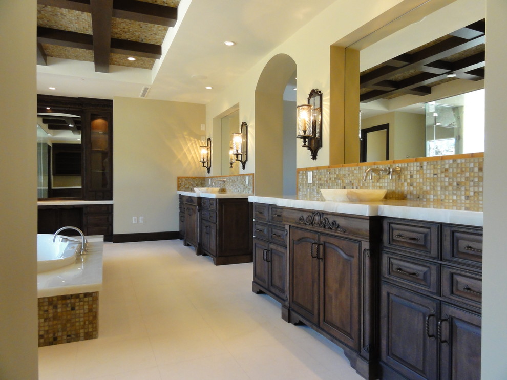 На фото: главная ванная комната в средиземноморском стиле с настольной раковиной, фасадами островного типа, темными деревянными фасадами, столешницей из оникса, накладной ванной и разноцветной плиткой